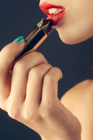 female hands with tender skin and blue manicure holding rose flower with soft petals red color in lipstick near sexy lipsの写真素材