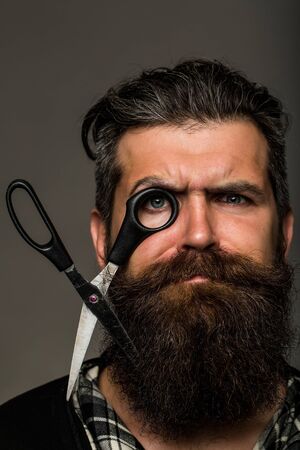 young handsome bearded man with long beard moustache and brunette hair holding hairdresser or barber...