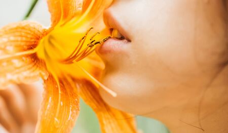 Sensual rosy lips on pretty woman face kiss bright orange lily flower blossoming on sunny dayの写真素材