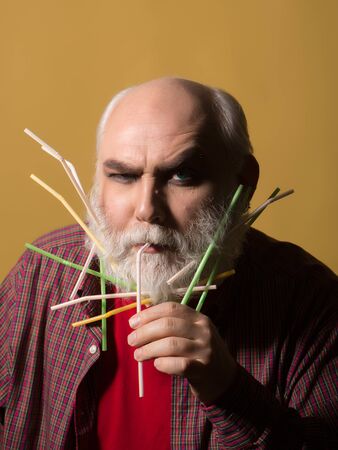 Old bearded man with many drinking straws in long grey beard on serious face in red checkered shirt...