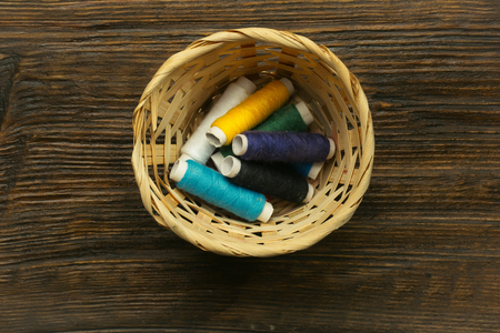 Many bobbins of bright colorful cotton threads for sewing laying in straw basket on wooden backgroundの写真素材
