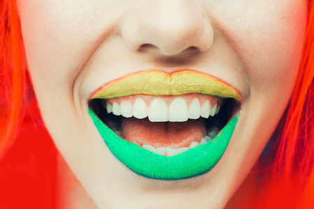 pretty sexy female lips with bright green and yellow lipstick on open mouth on smiling face with soft skin and orange hair, closeupの写真素材