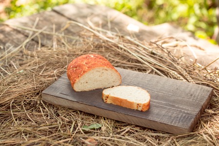 Freshly baked loaf of wheat bread and cut slice on wooden board with spikelet on straw or hay backgroundの写真素材