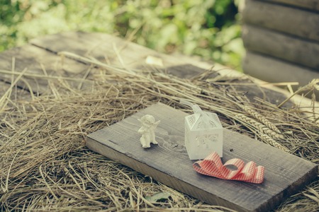 white angel valentines day cupid figure present or gift box and red ribbon bow on wooden board on straw or hay background outdoorの写真素材