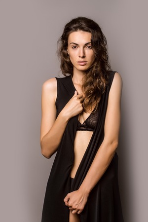 young sexy woman with pretty face and long brunette curly hair in black bra and panties has slim body in studio on grey backgroundの写真素材