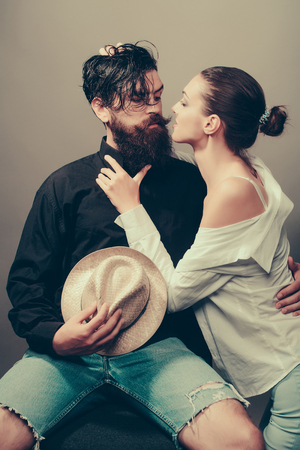 young sexy couple of woman with glamour makeup on pretty face in stylish shirt and bra kiss handsome bearded man with long beard and wet hair holding straw hat in studio on grey backgroundの写真素材