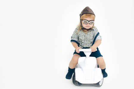 small boy kid driver or pilot sitting on plastic toy cat in stylish shirt helmet or hat and glasses isolated on white background, copy spaceの写真素材