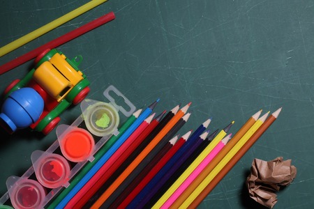 many colorful stationary of pencils for drawing art different colors laying on green school blackboard or desk with plastic car toy paint and paper, copy spaceの写真素材