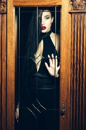 Attractive girl in a black dress with red lipstick trapped behind the glass doorの写真素材