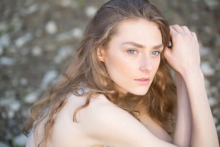 Pretty girl young woman with natural blond curly long hair and beautiful face poses outdoor on summer dayの写真素材