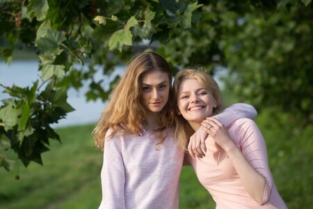 Two young girls best friends hug and smile on summer day near river in green parkの写真素材