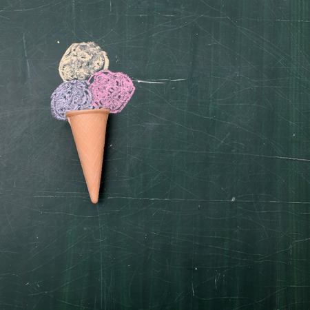 Tasty ice cream drawing with colorful chalk in waffle cone on green school chalkboard background...