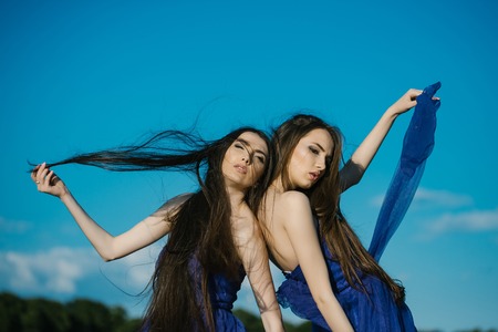 young pretty women with long windy hair in elegant violet dresses sunny day outdoor on blue sky backgroundの写真素材
