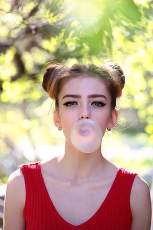 young pretty woman with chewing gum in the garden with fresh spring leaves on trees on blurred...