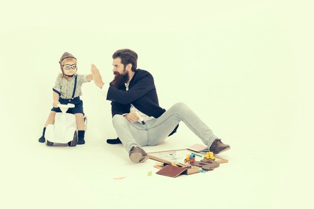 small boy kid driver or pilot sitting on plastic toy cat in stylish shirt with bearded man father with beard near school appliances of blackboard letter pen and paper isolated on white backgroundの写真素材