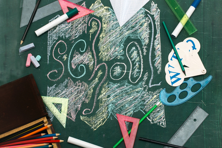 School text word drawing on green blackboard with colorful chalk surrounded with colored triangle rules alphabet pencils in box and markersの写真素材