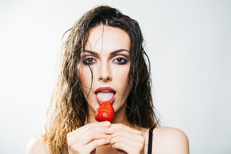 young woman with pretty face and wet hair holding red strawberry berry fruit in studio isolated on white backgroundの写真素材