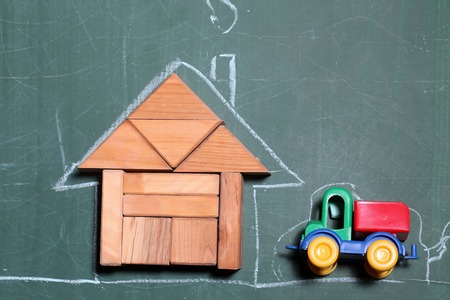 Creative house made of wooden blocks and drawing by chalk colored car toy near on green school blackboardの写真素材