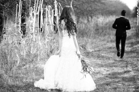Young newlywed couple of pretty woman in wedding dress and groom walking in forest decorated with ribbons, black and whiteの写真素材