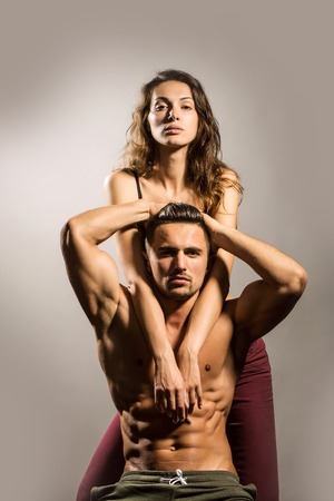 young sexy couple of pretty woman in black bra with wet hair and handsome macho man with muscular torso and athletic body in studio on grey backgroundの写真素材