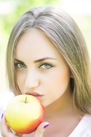 Young beautiful woman eats ripe tasty yellow apple outdoors on sunny summer dayの写真素材