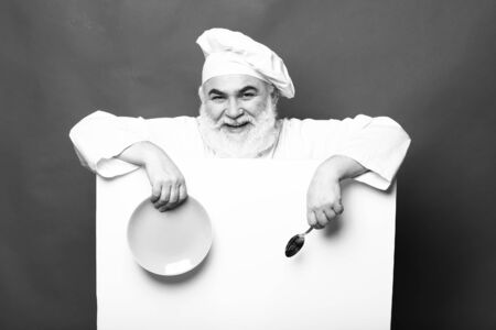 Happy bearded cook holding blank paper with spoon bottle and napkin, copy space, black and whiteの写真素材