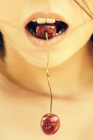 Red cherries pair hang from young woman mouth with rosy sensual lipsの写真素材