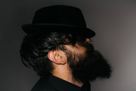 handsome bearded young man hipster or gentleman with long beard and mustache in stylish black retro hat on serious face in studio on grey background, portraitの写真素材