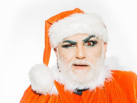 Santa claus bearded man magic person with bright makeup on surprised face with squinty eyes in red christmas coat and hat posing on white background studioの写真素材