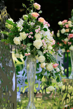 Wedding flower bouquet of beautiful natural tender pink white and creamy roses with green leaves in long glass vase floral decoration outdoorの写真素材