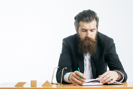young handsome bearded man scientist or professor with long beard and teacher glasses with book or notepaper sitting at table with wooden cubes isolated on white backgroundの写真素材