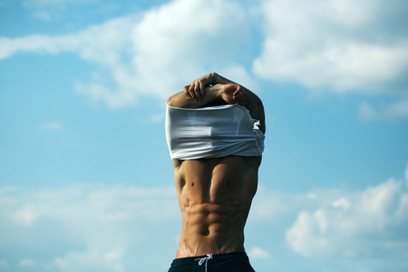 young macho man model athlete with muscular sexy body and wet bare chest outdoor on sky background undressing white shirtの写真素材