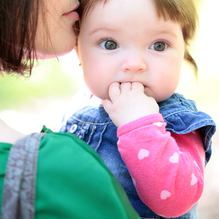 Small cute baby girl with pretty face and funny eyes on mothers hands sunny day outdoor on natural background closeupの写真素材