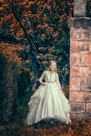 Pretty girl in white vintage dress poses near old stone house in autumn forestの写真素材