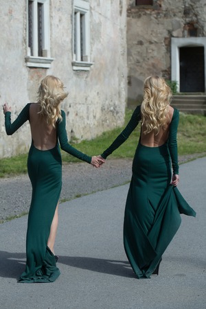 young pretty women with long lush curly blonde hair and sexy bodies in green dresses walking near stony building with windows outdoorの写真素材