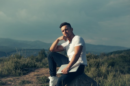 Young handsome man with muscular sexy body sitting with laptop outdoor sunny day on blue sky backgroundの写真素材