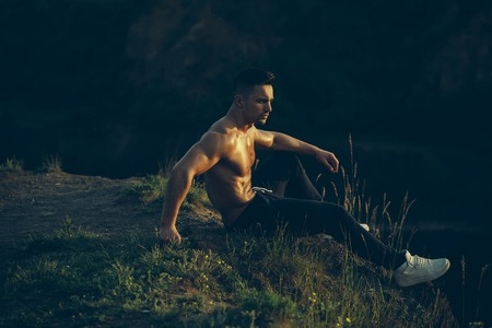 young macho man model athlete with muscular sexy body and wet bare chest outdoor on hill with city landscapeの写真素材