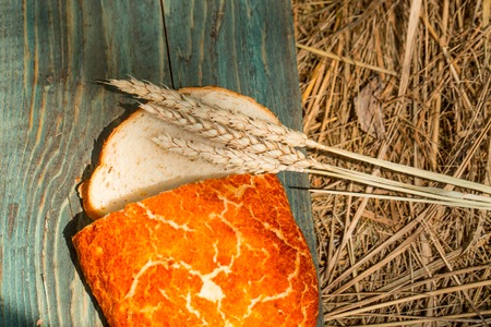 Freshly baked loaf of wheat bread and cut slice on wooden board with spikelet on straw or hay backgroundの写真素材