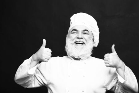 Bearded man cook with smiling face in chef hat with thumb up in studio, black and whiteの写真素材