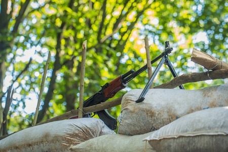 Military rifle standing on sandbags block post in forest on background of green treesの写真素材