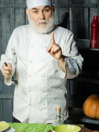 Bearded man cook in studio preparing food with sauce on wooden backgroundの写真素材