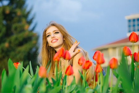 happy beautiful young slender girl is sitting with red tulipsの写真素材
