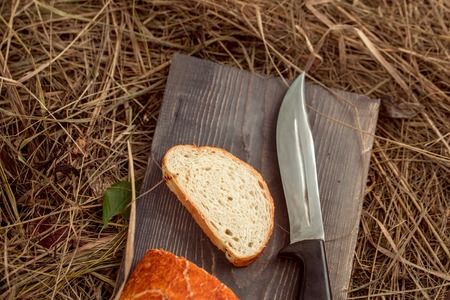 Freshly baked loaf of wheat bread and cut slice on wooden board on straw or hay background with glass cup of milk near sharp knifeの写真素材