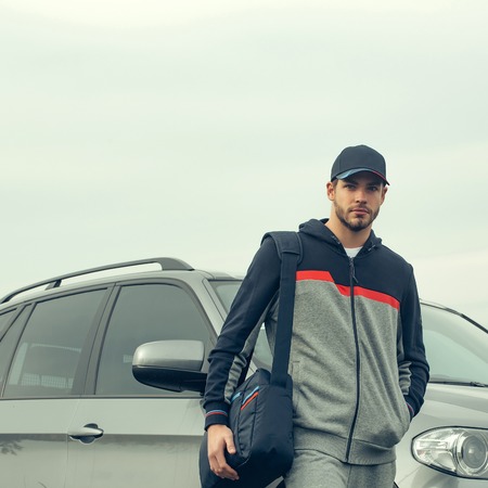 Young guy with beard on his serious face in casual hoody dark blue baseball cap on head and sports...