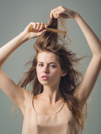 young woman with slim body pretty face and brunette long hair in dress holding hairbrush standing in studio on grey backgroundの写真素材