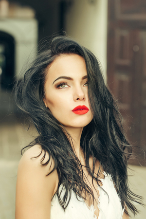 young woman or girl with long black brunette hair and red lips on pretty face outdoor portrait on building backgroundの写真素材