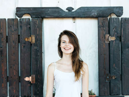 Beautiful girl with long brunette hair smiles outdoor against vintage shuttersの写真素材