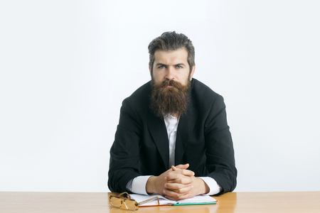 young handsome bearded man scientist or professor with long beard and teacher glasses with book or notepaper sitting at table isolated on white backgroundの写真素材