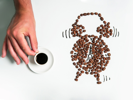 human hand holds white cup of coffee drink or beverage with roasted brown beans in alarm clock isolated on white backgroundの写真素材