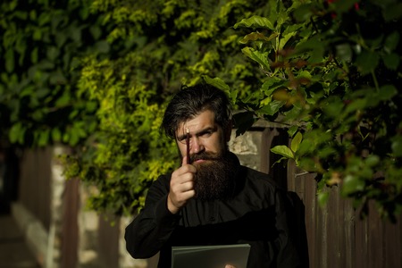 handsome sexy bearded young man hipster with long beard and mustache has stylish hair on serious hairy face sunny day outdoor holding note and pencil on green natural backgroundの写真素材
